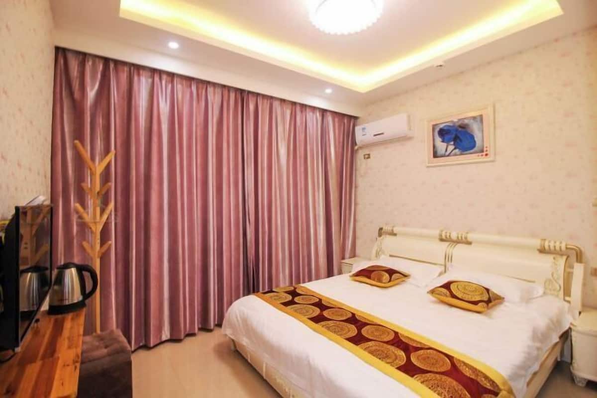 Una habitación de hotel con cama, una mesita de noche de madera, perchero y un cuadro en la pared.