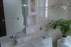 Un baño con lavamanos, espejo, toallero, inodoro y una planta en maceta.