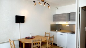 Une cuisine compacte avec des meubles blancs, une table à manger en bois et un lave-vaisselle encastré.