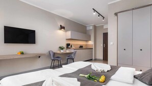 A modern hotel room with a bed, a small kitchenette, a TV mounted on the wall, and a wardrobe.