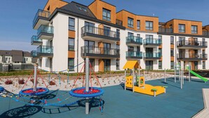 A modern apartment building with balconies, a playground, and a clear sky.