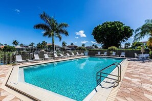 A rectangular swimming pool with clear blue water, surrounded by lounge chairs and palm trees. - Waterfront 2BR, 2BA condo with heated pool, WiFi, and marina access. (Marco Island)