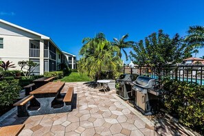 A patio with hexagonal tiles, picnic tables, a barbecue grill, and a pool. - Waterfront 2BR, 2BA condo with heated pool, WiFi, and marina access. (Marco Island)