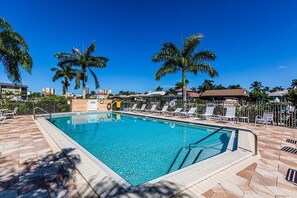 A swimming pool with lounge chairs and palm trees. - Waterfront 2BR, 2BA condo with heated pool, WiFi, and marina access. (Marco Island)