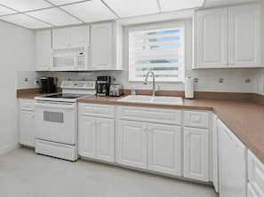 A kitchen with white cabinets, a microwave, a stove, a sink, and a window with blinds.