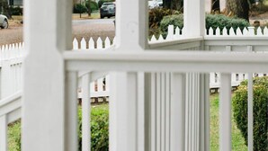 A white wooden porch with a picket fence, surrounded by trees and a street view. - Leave the day behind. Walk downtown. Wake up feeling at home. (Montgomery)