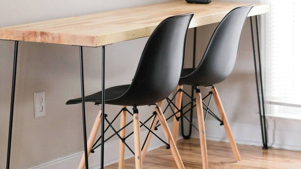 A dining area with a wooden table, two black chairs, and a television mounted on the wall. - Leave the day behind. Walk downtown. Wake up feeling at home. (Montgomery)