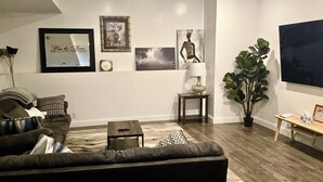 A living room with a dark brown sofa, a small coffee table, a lamp, a TV, and a large potted plant. - Gardner 5 bedroom 3 bath home. Family friendly and long stay  (Gardner)
