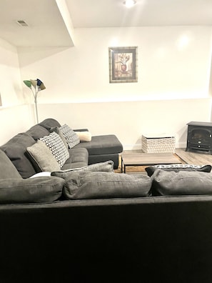 Uma sala de estar moderna com um sofá cinza escuro, almofadas estampadas, uma mesinha de apoio e um quadro na parede.