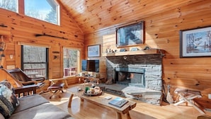 A cozy cabin interior with a stone fireplace, wooden walls, and a comfortable seating area. - Deer Ridge - 3BR, 3BA Cabin w/ Hot Tub, Firepit (Maggie Valley)