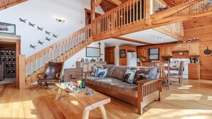 A wooden interior with a staircase, a sofa, a coffee table, and a kitchen area. - Deer Ridge - 3BR, 3BA Cabin w/ Hot Tub, Firepit (Maggie Valley)