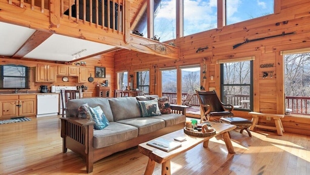 A cabin with a wooden interior, a sofa, a dining table, and a kitchen area. - Deer Ridge - 3BR, 3BA Cabin w/ Hot Tub, Firepit (Maggie Valley)