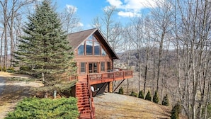 A log cabin with a balcony, surrounded by trees and a hilly landscape. - Deer Ridge - 3BR, 3BA Cabin w/ Hot Tub, Firepit (Maggie Valley)