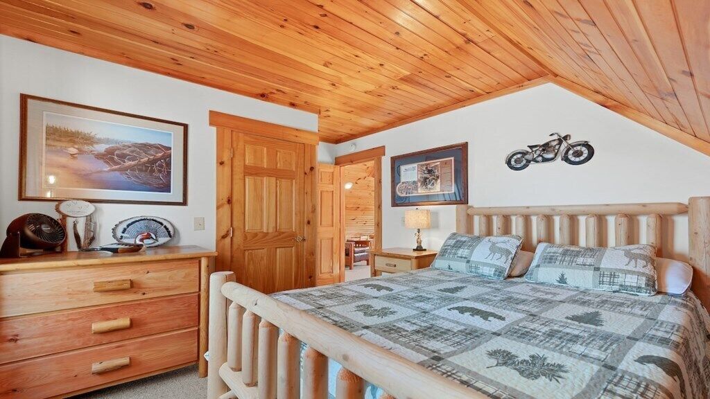 Une chambre avec un plafond en bois, un lit recouvert d’une courtepointe, une commode et un autocollant représentant une moto sur le mur.