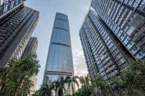 A tall, modern skyscraper with a curved glass facade, surrounded by other high-rise buildings and palm trees. - Grace Apartment (Shenzhen)
