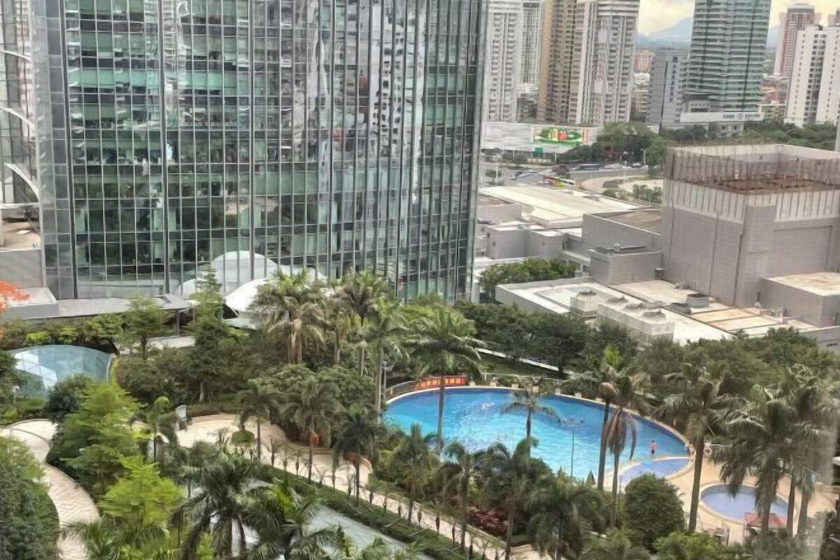 A high-rise building with a glass facade, a swimming pool surrounded by palm trees, and a view of the cityscape.