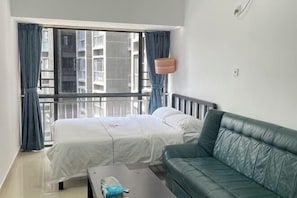 A room with a bed, a green sofa, a small table, and a window with curtains.
