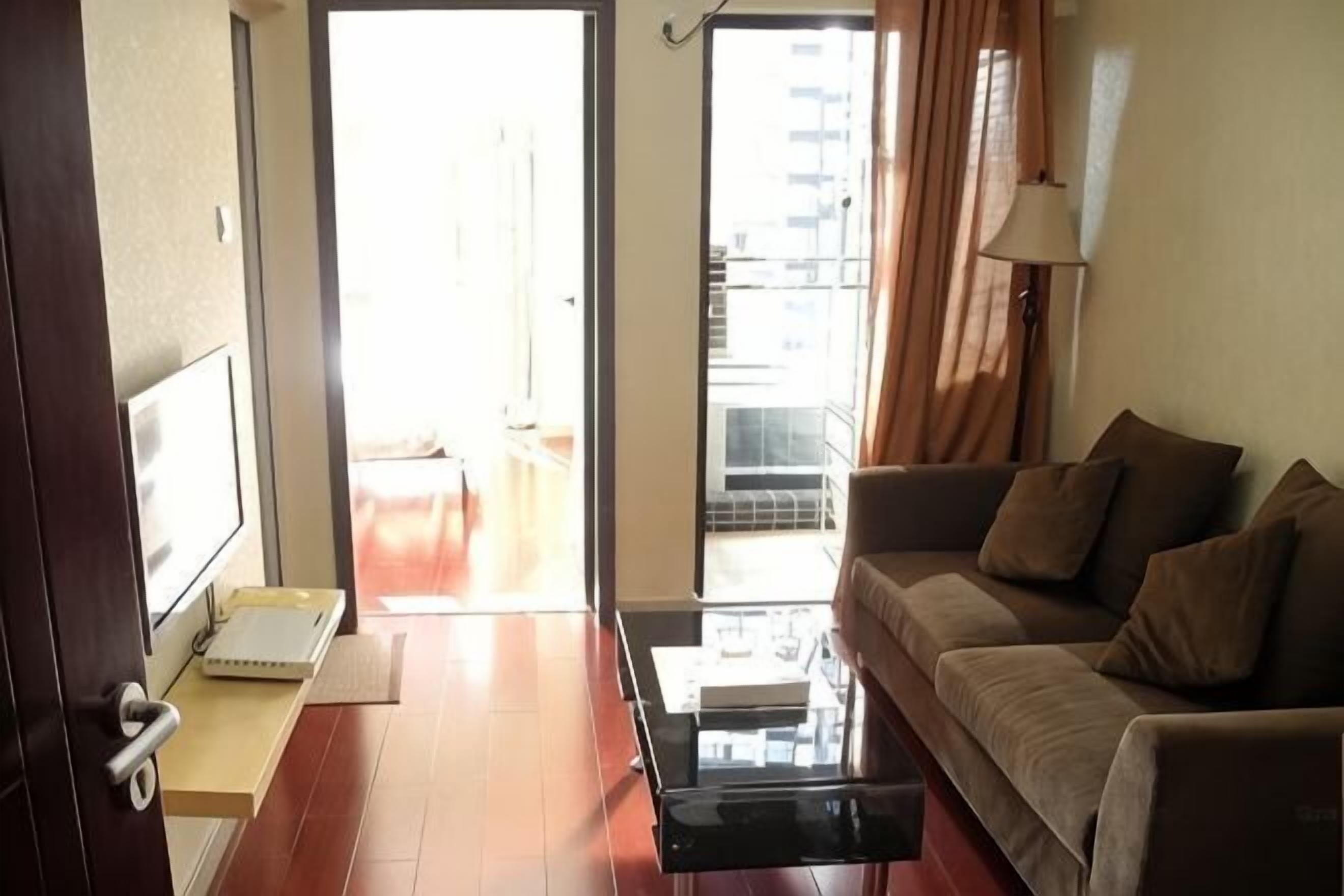 A living room with a sofa, a coffee table, a TV, and a sliding door leading to a balcony.