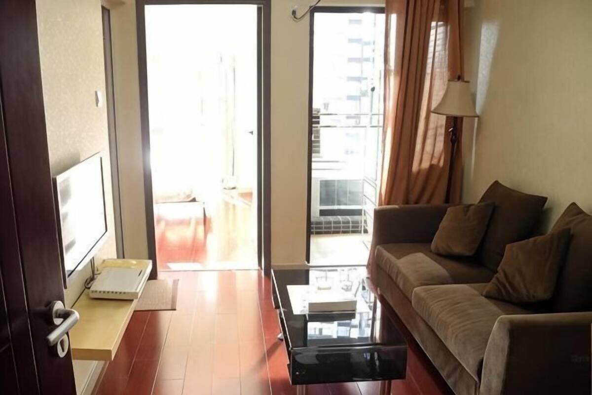 A living room with a sofa, a coffee table, a TV, and a sliding door leading to a balcony.