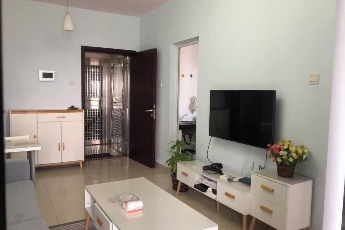 A modern living room with a flat-screen TV, a dining table, a sofa, and a cabinet.