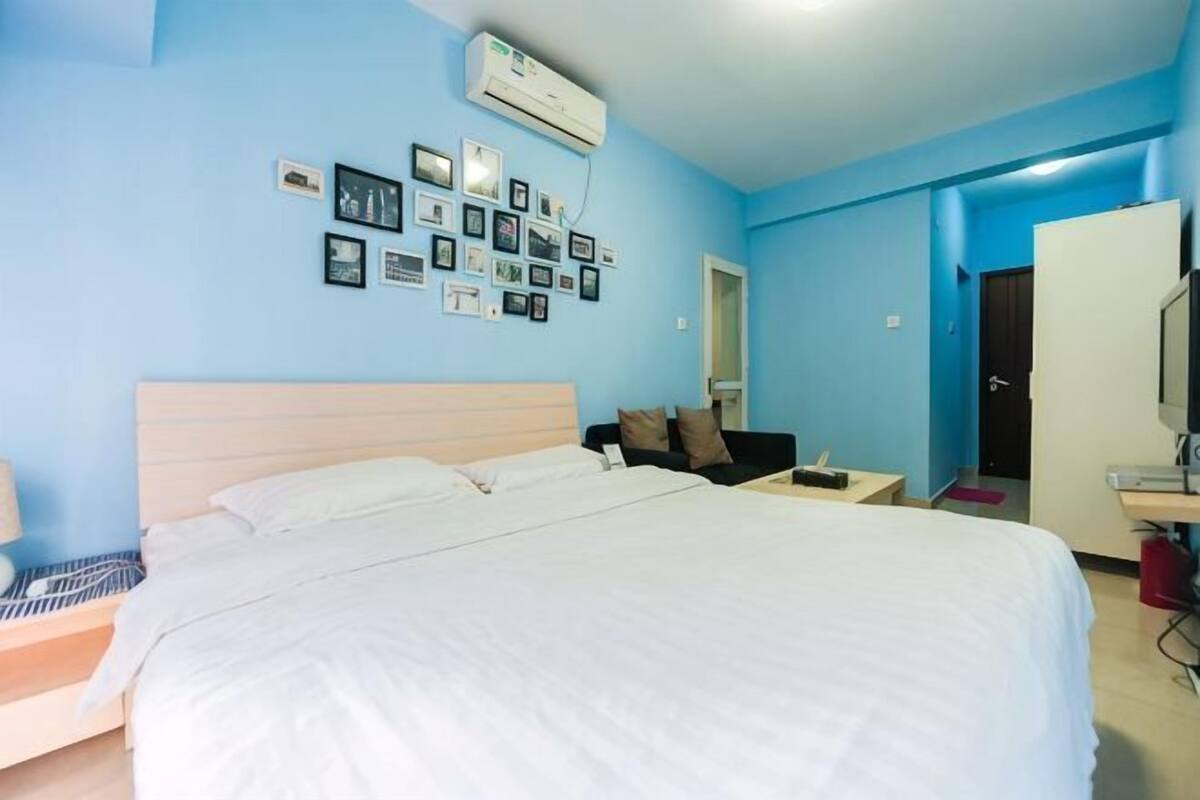A hotel room with a large bed, a desk, a chair, a TV, and a wardrobe.