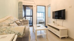 A living room with a sofa, a coffee table, a TV, and a balcony door. - Grace Apartment (Shenzhen)