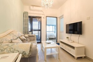 A living room with a sofa, a coffee table, a TV, and a balcony door. - Grace Apartment (Shenzhen)