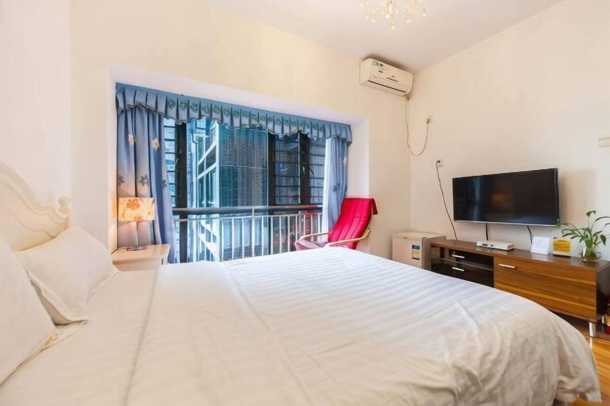 A hotel room with a bed, a TV, a balcony with a chair, and a window with curtains.