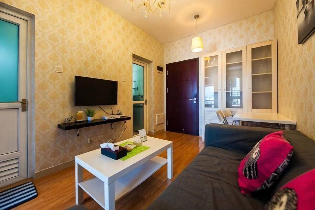 A living room with a TV, a coffee table, a sofa, and a door leading to another room.