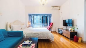 A bedroom with a bed, a TV, a window with curtains, a red chair, and a wooden floor. - Grace Apartment (Shenzhen)