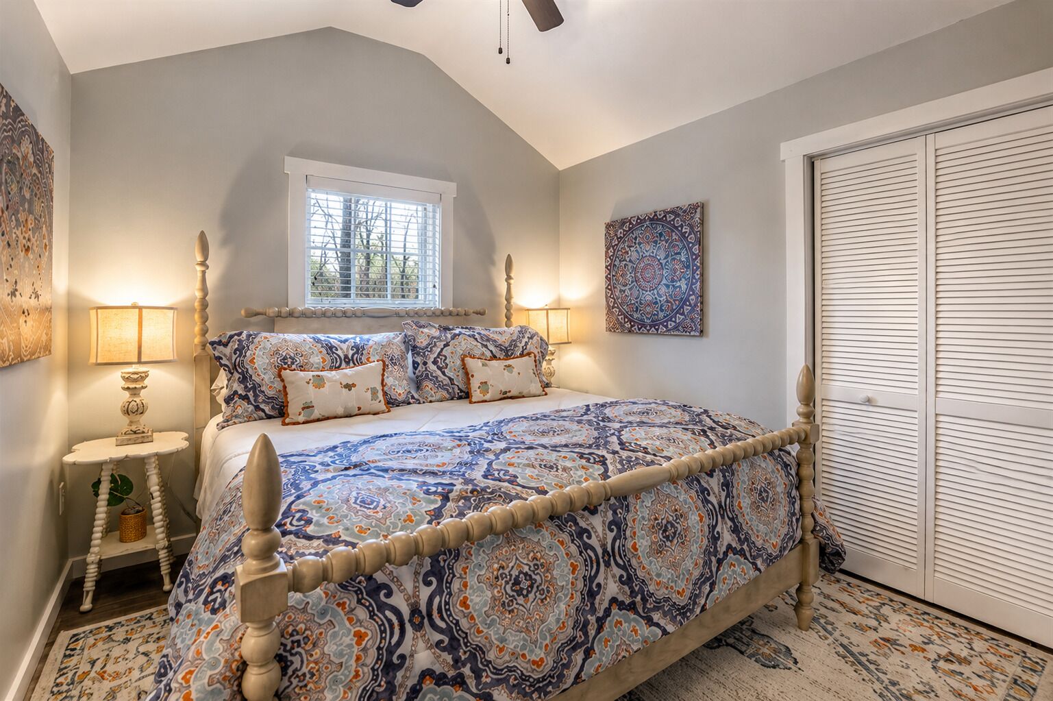 A bedroom with a large bed, a window, a bedside table with a lamp, and a wardrobe.