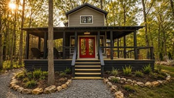 A cabin with a red door, a porch, and a gravel path leading to it.
