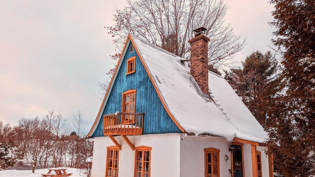 Una casa cubierta de nieve con fachada azul y blanca, un balcón de madera y una chimenea.
