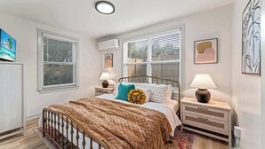 Une chambre à coucher comprenant un lit, deux tables de chevet, une fenêtre et un climatiseur fixé au mur.