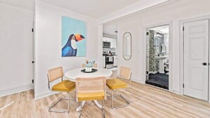 Un coin repas avec une table ronde, quatre chaises, un tableau et une cuisine en arrière-plan.