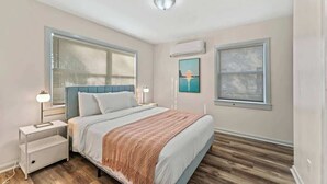 Une chambre à coucher avec un lit, des tables de chevet, une lampe, un climatiseur et une fenêtre.