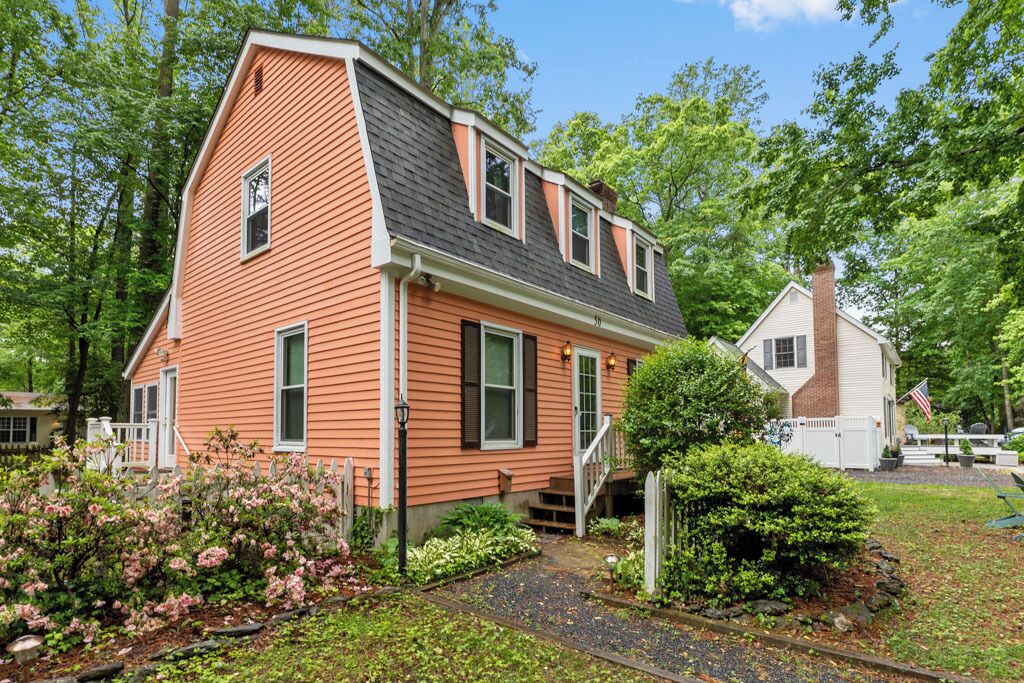 A two-story house with a steeply pitched roof, a front porch, and a well-maintained garden with flowering plants.