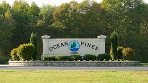 Placa de Ocean Pines, com um logotipo mostrando uma montanha e uma onda, cercada por vegetação e um muro de pedra.