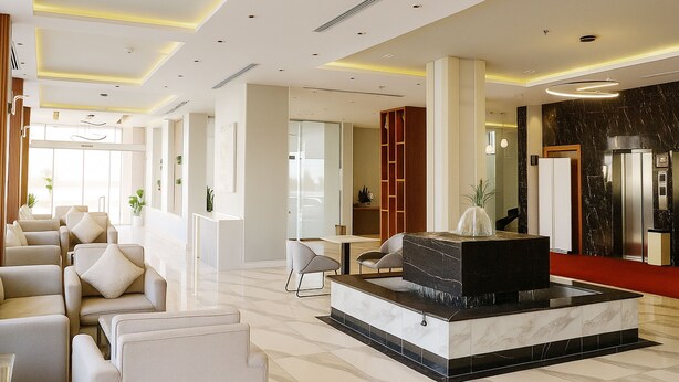 Un moderno vestíbulo de hotel con un mostrador de recepción de mármol, zona de estar y un espejo grande.