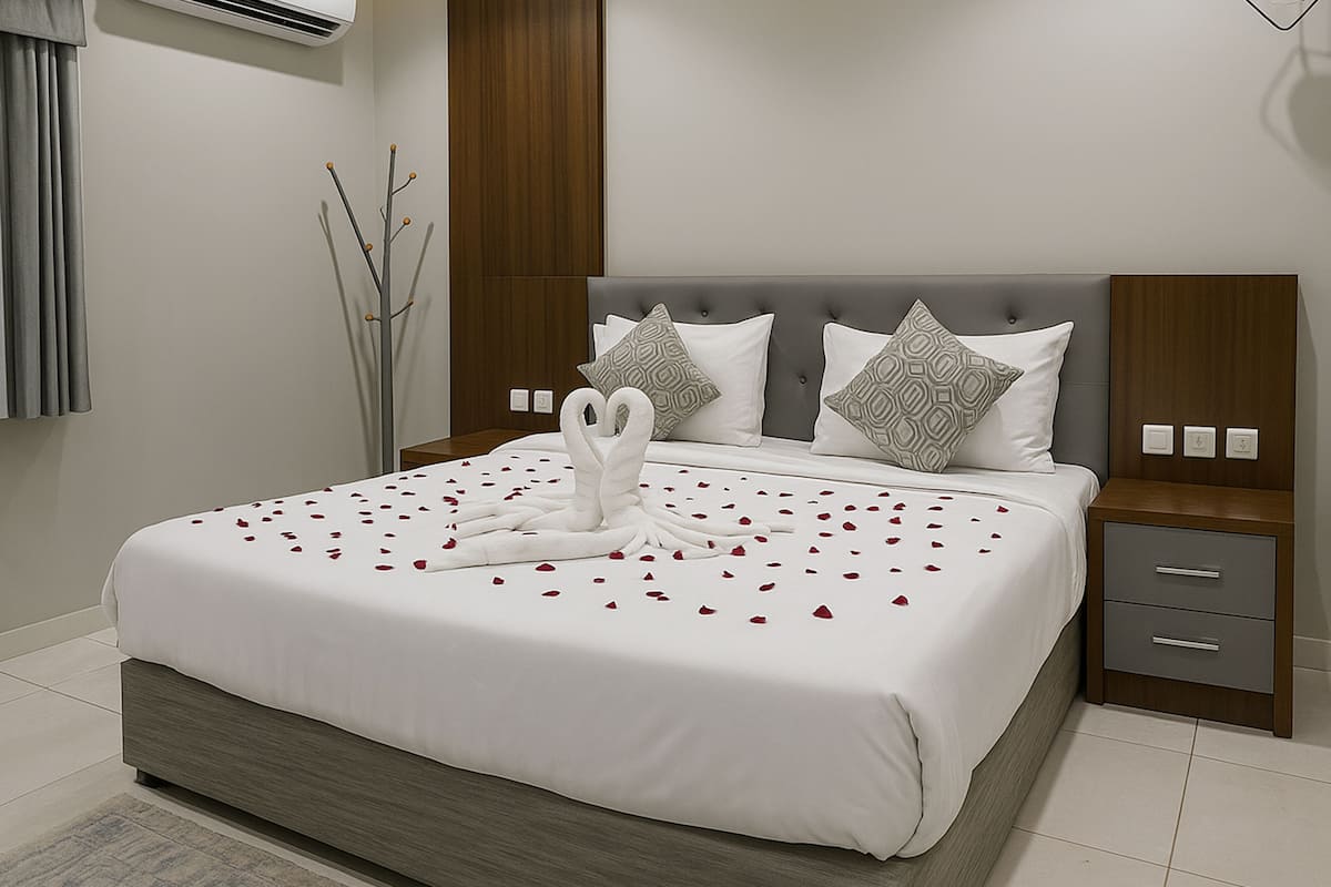 Una habitación de hotel moderna con una cama grande, ropa de cama gris y blanca, un cabecero de madera y una mesita de noche con cajones.