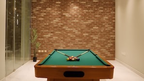 Una mesa de billar en una habitación con pared de ladrillo y puertas de vidrio.