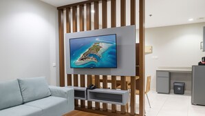 Una sala de estar moderna con un televisor de pantalla plana montado sobre un panel de madera, un sofá azul claro, una mesa de centro de madera y una zona de cocina al fondo.