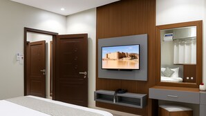 Habitación de hotel con cama, televisor montado en la pared, tocador con espejo y una puerta.