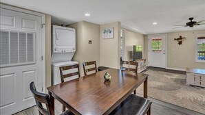 Un coin repas avec une table et des chaises en bois, un réfrigérateur blanc et un ventilateur de plafond.