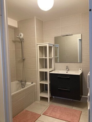Bathroom features a bathtub, handheld showerhead, and a vanity with a dark cabinet.