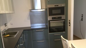 Eine moderne Küche mit Edelstahlgeräten, einem Einbauofen und einem Essbereich mit weißem Tisch und Stühlen.