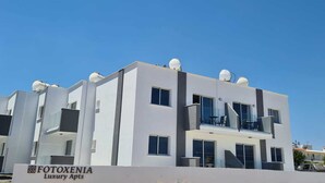 Een modern meerlaags gebouw met een bord waarop staat: "FOTOXENIA Luxury Apartments".