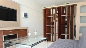 Een slaapkamer met een bed, een glazen tafel met twee wijnglazen, een kledingkast en een televisie.