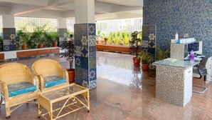 Un vestíbulo amplio con sillones de mimbre, una mesa de recepción y plantas en macetas.