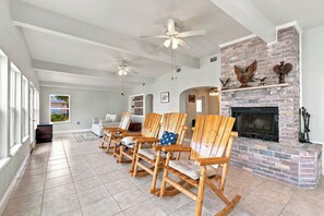 A living room with a fireplace, wooden chairs, and a ceiling fan. - Charming 3 Bedroom Water Front Bungalow (Pensacola Beach)